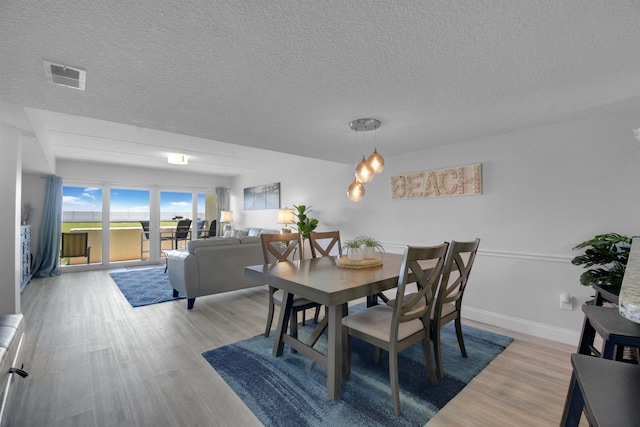 dining area featuring baseboards, a textured ceiling, visible vents, and light wood-style floors