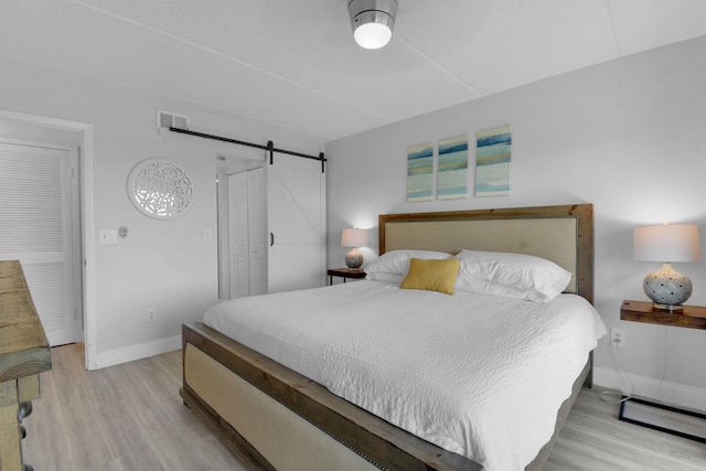 bedroom with baseboards, a barn door, visible vents, and light wood-style floors