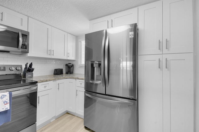 kitchen featuring appliances with stainless steel finishes, light wood-type flooring, white cabinets, and light stone countertops