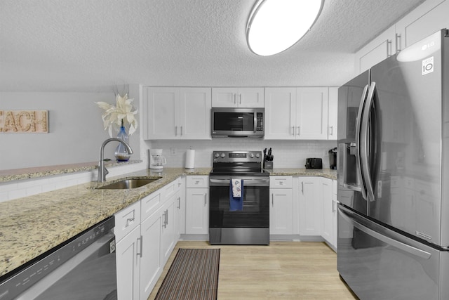 kitchen with stainless steel appliances, light wood-type flooring, a sink, and white cabinetry