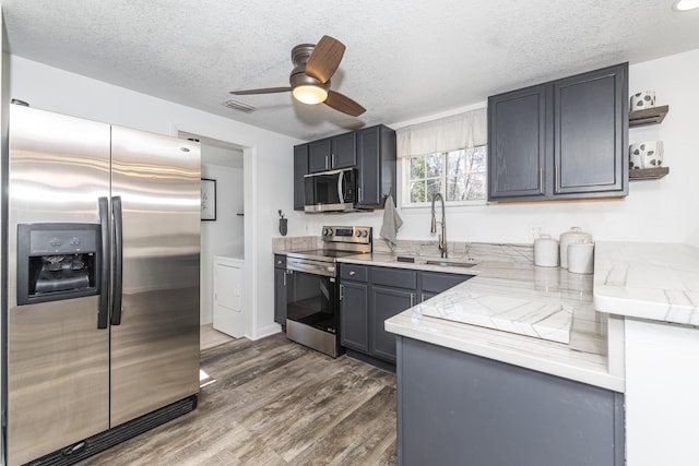 kitchen featuring sink, dark hardwood / wood-style flooring, stainless steel appliances, light stone countertops, and a textured ceiling