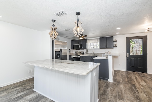 kitchen with light stone counters, dark hardwood / wood-style flooring, a kitchen island, pendant lighting, and stainless steel appliances