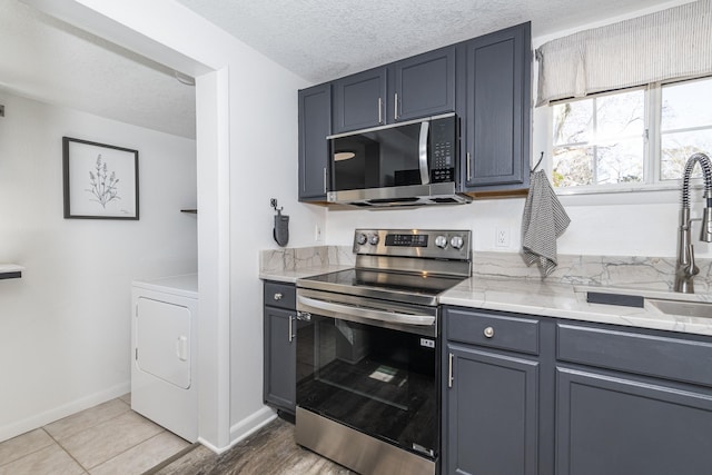 kitchen with sink, appliances with stainless steel finishes, gray cabinetry, a textured ceiling, and washer / clothes dryer