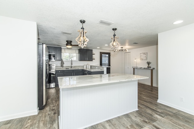 kitchen with sink, a center island, pendant lighting, stainless steel appliances, and light stone countertops