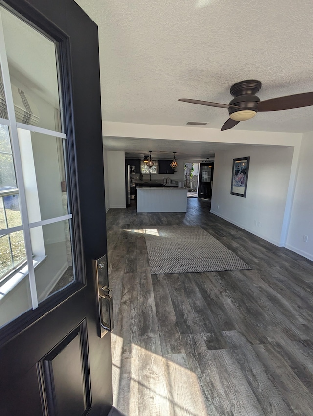 unfurnished living room featuring dark hardwood / wood-style flooring, ceiling fan, and a textured ceiling