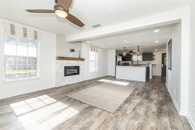 unfurnished living room with hardwood / wood-style flooring, ceiling fan, a fireplace, and a textured ceiling