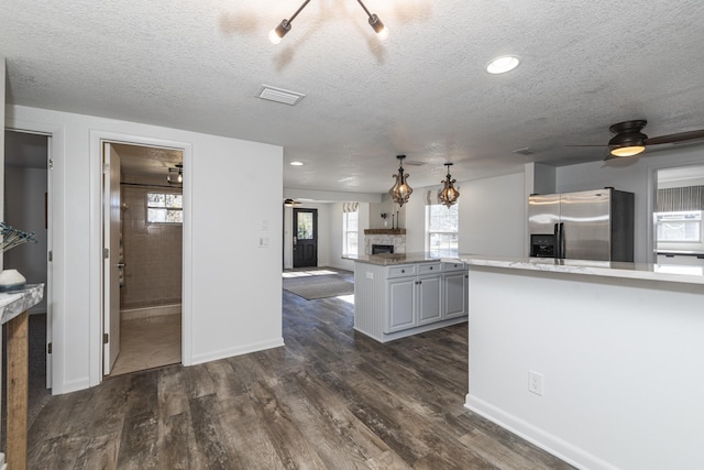 kitchen featuring gray cabinetry, dark hardwood / wood-style flooring, stainless steel fridge with ice dispenser, a stone fireplace, and kitchen peninsula