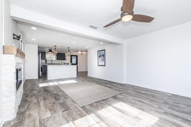 unfurnished living room featuring wood-type flooring, a stone fireplace, ceiling fan, and a textured ceiling