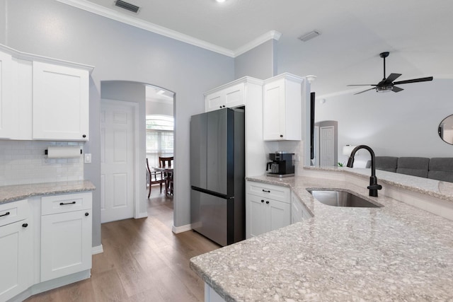 kitchen with sink, light stone counters, stainless steel refrigerator, ornamental molding, and white cabinets