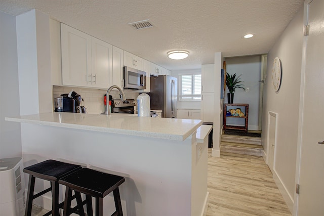 390 A1A Beach Blvd Unit 43, Saint Augustine Beach, FL 32080 - kitchen with stainless steel appliances, a peninsula, a textured ceiling, light wood-style floors, and backsplash