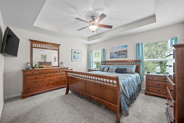 bedroom with a tray ceiling, light colored carpet, and a textured ceiling