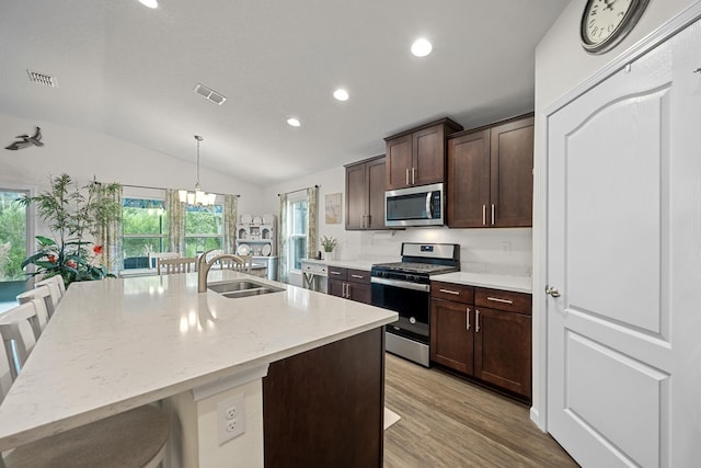 kitchen with appliances with stainless steel finishes, sink, a kitchen breakfast bar, hanging light fixtures, and a center island with sink