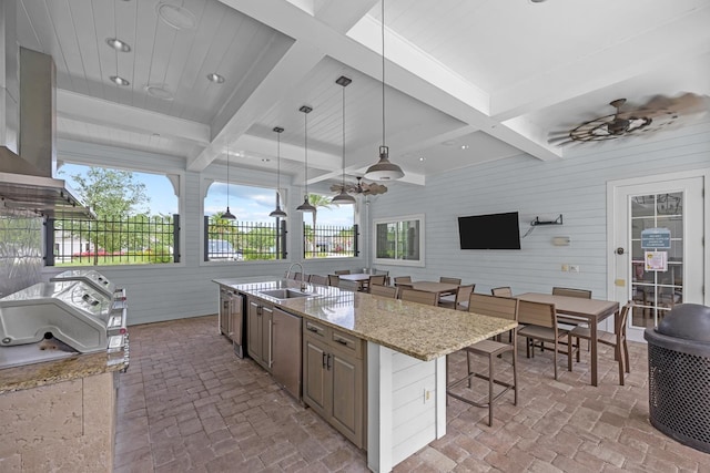 kitchen with sink, light stone counters, decorative light fixtures, beamed ceiling, and a kitchen island with sink