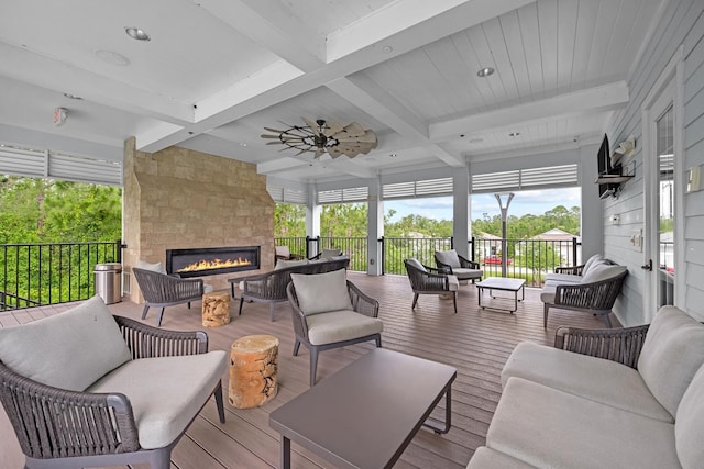 sunroom / solarium featuring beamed ceiling, a large fireplace, and ceiling fan