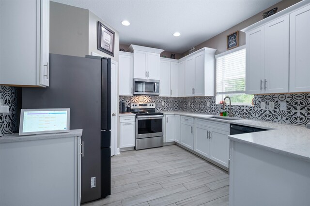 201 N Saxxon Rd, Saint Augustine, FL 32092 - kitchen with backsplash, appliances with stainless steel finishes, white cabinetry, a sink, and light wood-style flooring