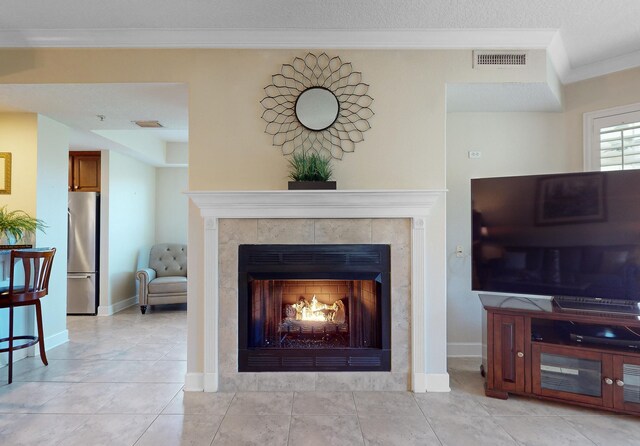 living area with a tiled fireplace, baseboards, visible vents, and ornamental molding