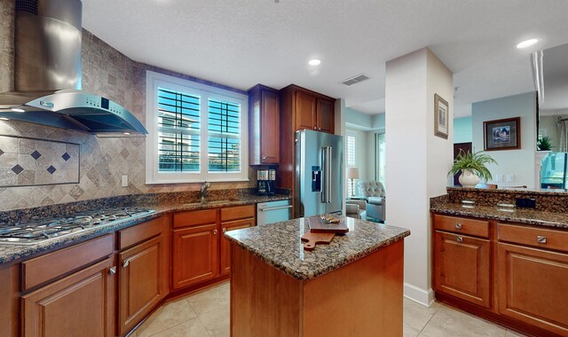 kitchen with dark stone countertops, stainless steel appliances, wall chimney exhaust hood, and a sink