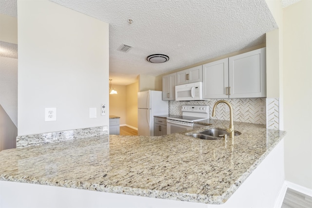 kitchen featuring light stone counters, a peninsula, white appliances, visible vents, and decorative backsplash