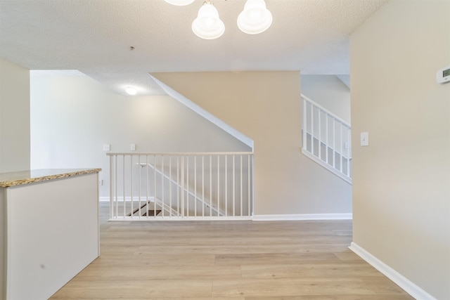 interior space with a textured ceiling, light wood finished floors, a chandelier, and baseboards