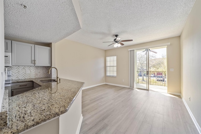 kitchen with light stone counters, decorative backsplash, white microwave, a sink, and light wood-type flooring