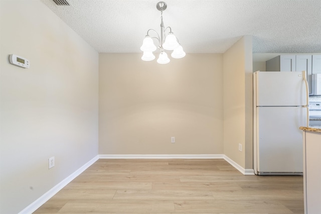unfurnished dining area with a textured ceiling, light wood-type flooring, and baseboards