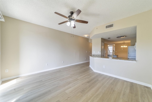 unfurnished living room featuring a textured ceiling, ceiling fan with notable chandelier, visible vents, baseboards, and light wood finished floors