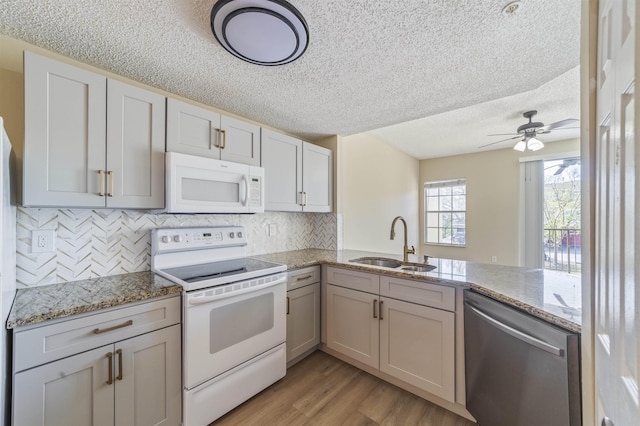 kitchen featuring light wood finished floors, backsplash, a sink, white appliances, and a peninsula