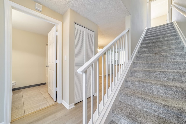 stairs featuring a textured ceiling, wood finished floors, and baseboards