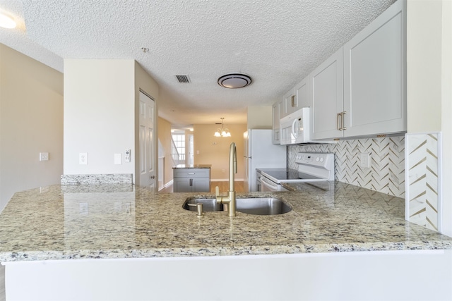 kitchen featuring visible vents, backsplash, a sink, white appliances, and a peninsula