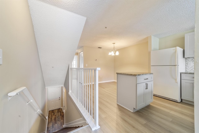 kitchen featuring decorative light fixtures, light wood-type flooring, freestanding refrigerator, and an inviting chandelier