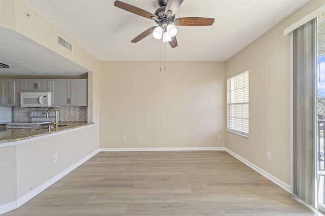 empty room with light wood-style floors, baseboards, visible vents, and a textured ceiling