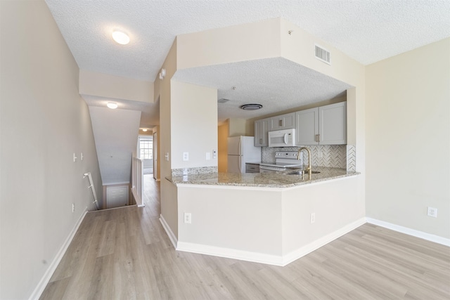 kitchen with white appliances, visible vents, decorative backsplash, light wood-type flooring, and a sink