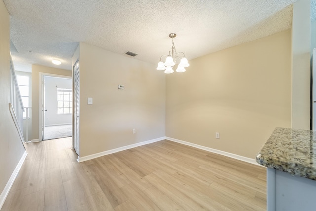 unfurnished dining area with baseboards, visible vents, a notable chandelier, and light wood finished floors