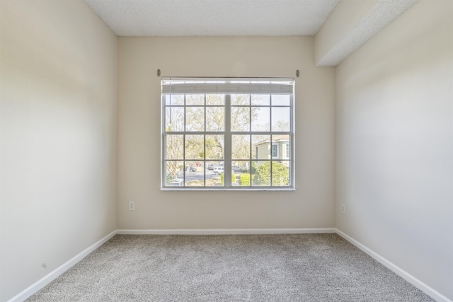 carpeted spare room featuring a textured ceiling and baseboards