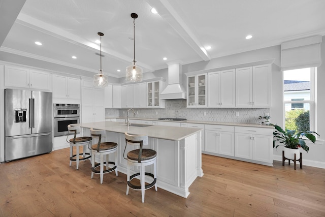 kitchen with a center island with sink, stainless steel appliances, wall chimney exhaust hood, and white cabinetry