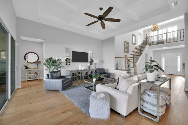 living room with coffered ceiling, light wood-type flooring, a towering ceiling, ceiling fan with notable chandelier, and beamed ceiling