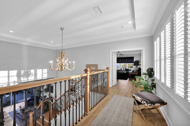 corridor featuring light wood-type flooring, an inviting chandelier, crown molding, and a raised ceiling