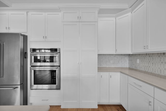 kitchen with appliances with stainless steel finishes, white cabinetry, backsplash, light hardwood / wood-style flooring, and crown molding