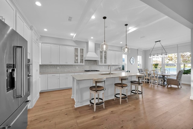 kitchen featuring appliances with stainless steel finishes, custom exhaust hood, white cabinets, and an island with sink