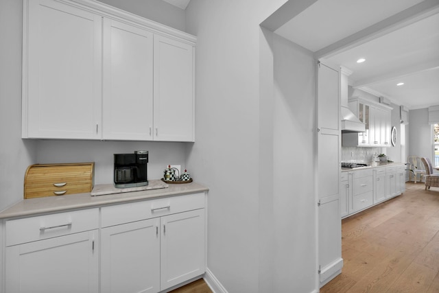 kitchen featuring custom exhaust hood, stainless steel gas cooktop, light wood-type flooring, and white cabinetry