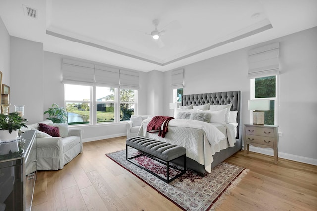 bedroom with a raised ceiling, ceiling fan, and light hardwood / wood-style floors