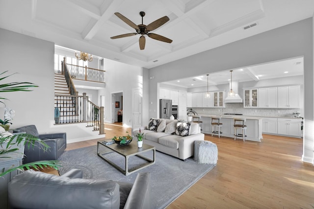 living room featuring light hardwood / wood-style floors, ceiling fan with notable chandelier, beam ceiling, and coffered ceiling