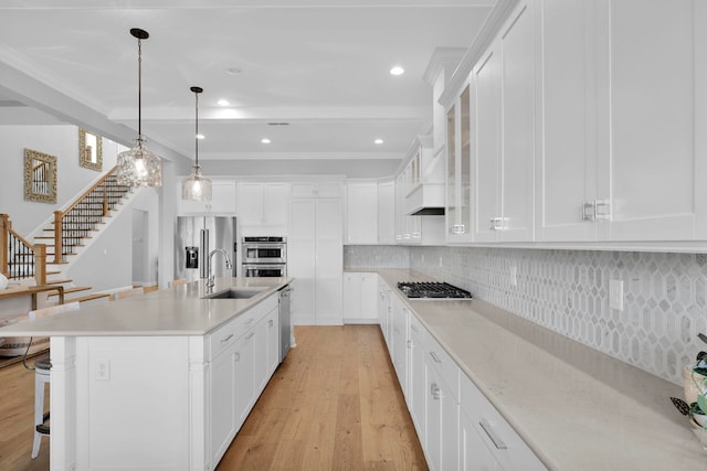 kitchen with white cabinets, appliances with stainless steel finishes, decorative light fixtures, sink, and a center island with sink