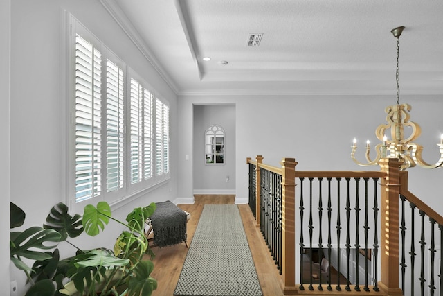 hall featuring light wood-type flooring, an inviting chandelier, ornamental molding, and a tray ceiling