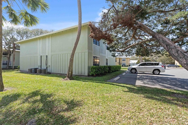 view of side of property with a yard, uncovered parking, and cooling unit