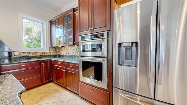 kitchen with stainless steel appliances, backsplash, crown molding, dark stone counters, and light tile patterned floors