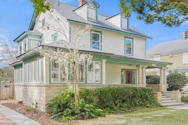 view of front of property featuring covered porch, a chimney, and fence