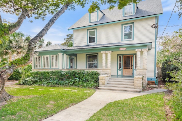 view of front of property featuring a front lawn, covered porch, and a shingled roof