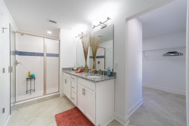 bathroom with vanity, a stall shower, a spacious closet, a textured ceiling, and visible vents