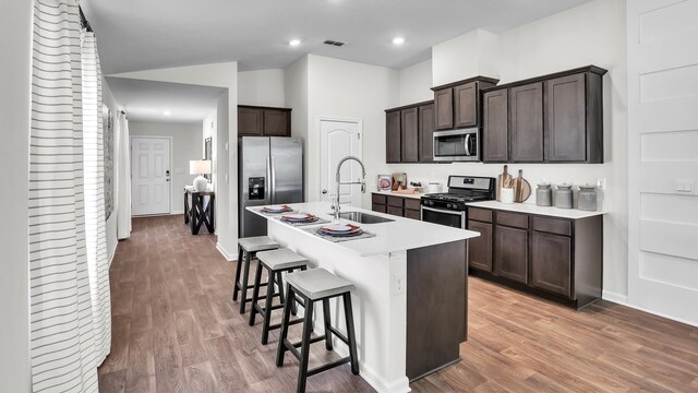 804 Grand Reserve Dr, Bunnell, FL 32110 - kitchen with a kitchen breakfast bar, dark brown cabinetry, appliances with stainless steel finishes, light wood-type flooring, and a sink